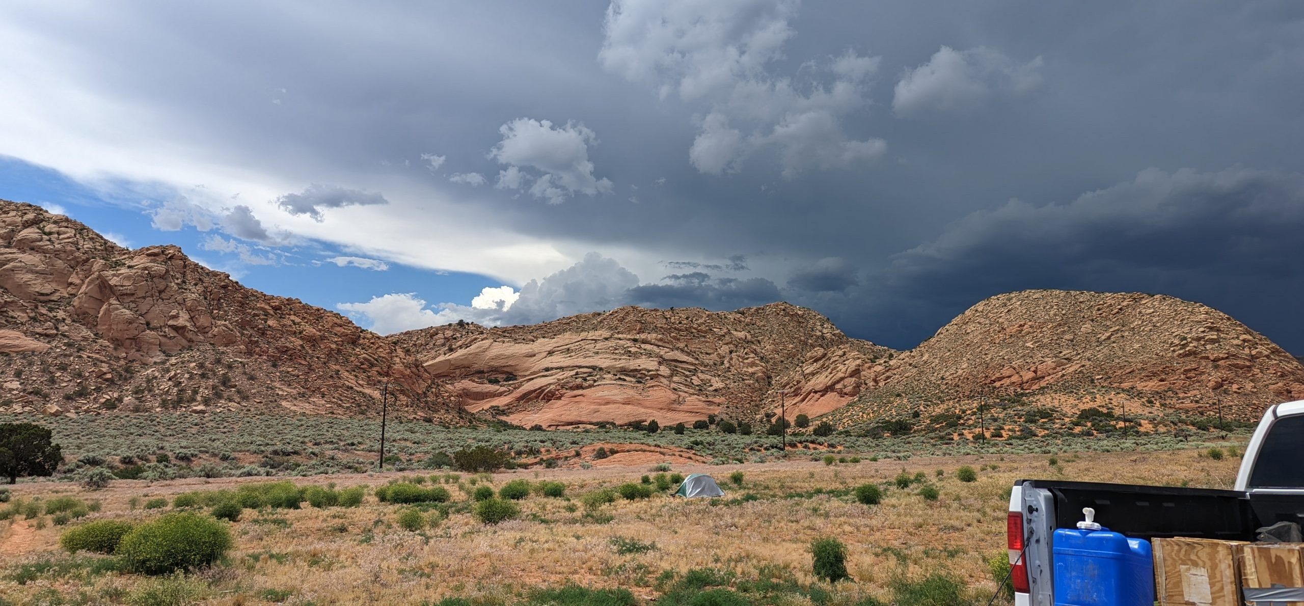 Photo of a desert landscape with dark clouds in the sky and a field truck in the foreground.