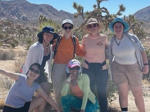 Photo of a group of women in hiking gear in front of a Joshua tree